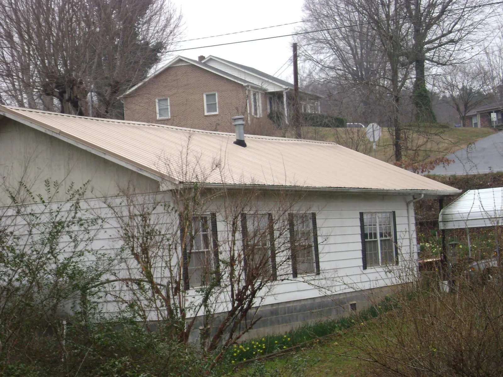 Tan metal roof on a white sided house set into a hillside — Commercial Roofing by Roofing Brothers in Warsaw