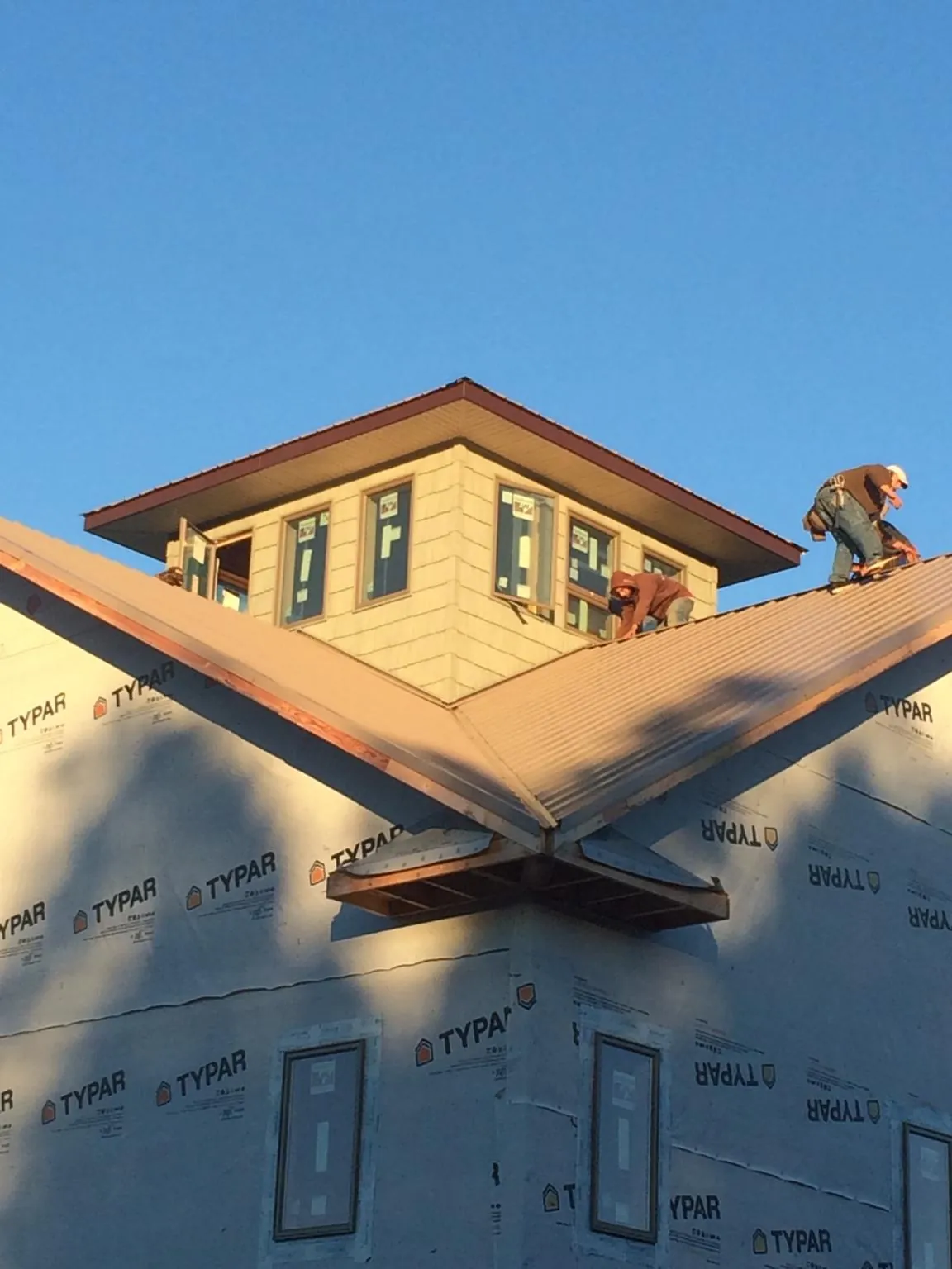 Roofers working around a rooftop cupola on a new metal roof at sunset — Roof Waterproofing in Warsaw by Roofing Brothers